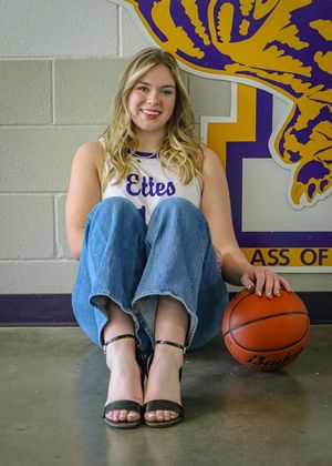 Student athlete in Ettes uniform sits casually with basketball against school mascot wall decoration.