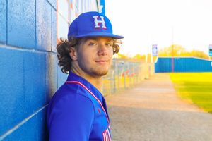 Baseball player in blue uniform leaning against blue wall at baseball field.