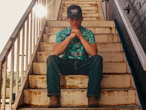 Person in teal patterned shirt sitting on concrete stairs with hands clasped.