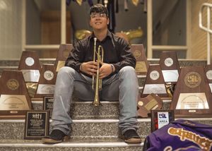 Musician sitting on steps with trumpet surrounded by trophy awards.