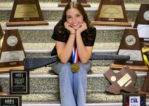 Student posing with academic awards and trophies on display steps.