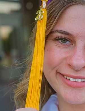 Smiling young woman in yellow graduation tassel and cap celebrating her 2025 graduation ceremony outdoors.