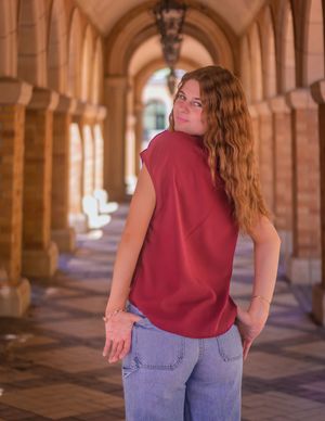 Person in a burgundy top and jeans poses in an ornate stone archway corridor with dramatic lighting.
