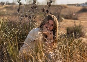 Young woman smiling among golden wild grasses in a sunlit field during golden hour.