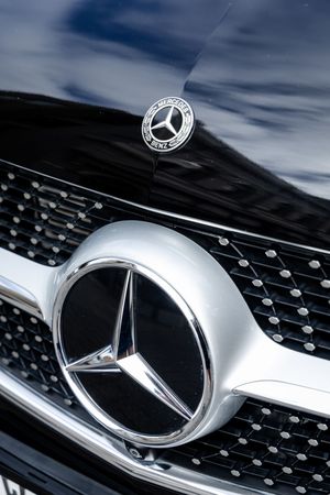 Close-up detail shot of a Mercedes-Benz luxury car grille showing the iconic three-pointed star emblem on a black mesh background.