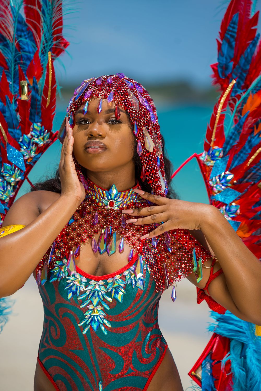 Carnival masquerade costume with intricate beadwork and red feathers photographed on tropical beach.