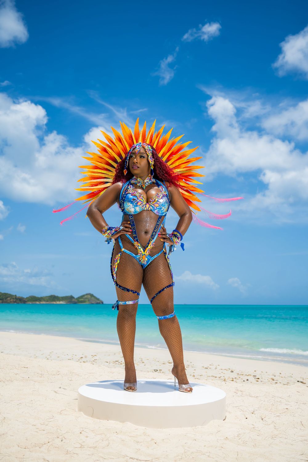 Carnival dancer in blue costume and orange feathered headpiece poses on tropical beach.