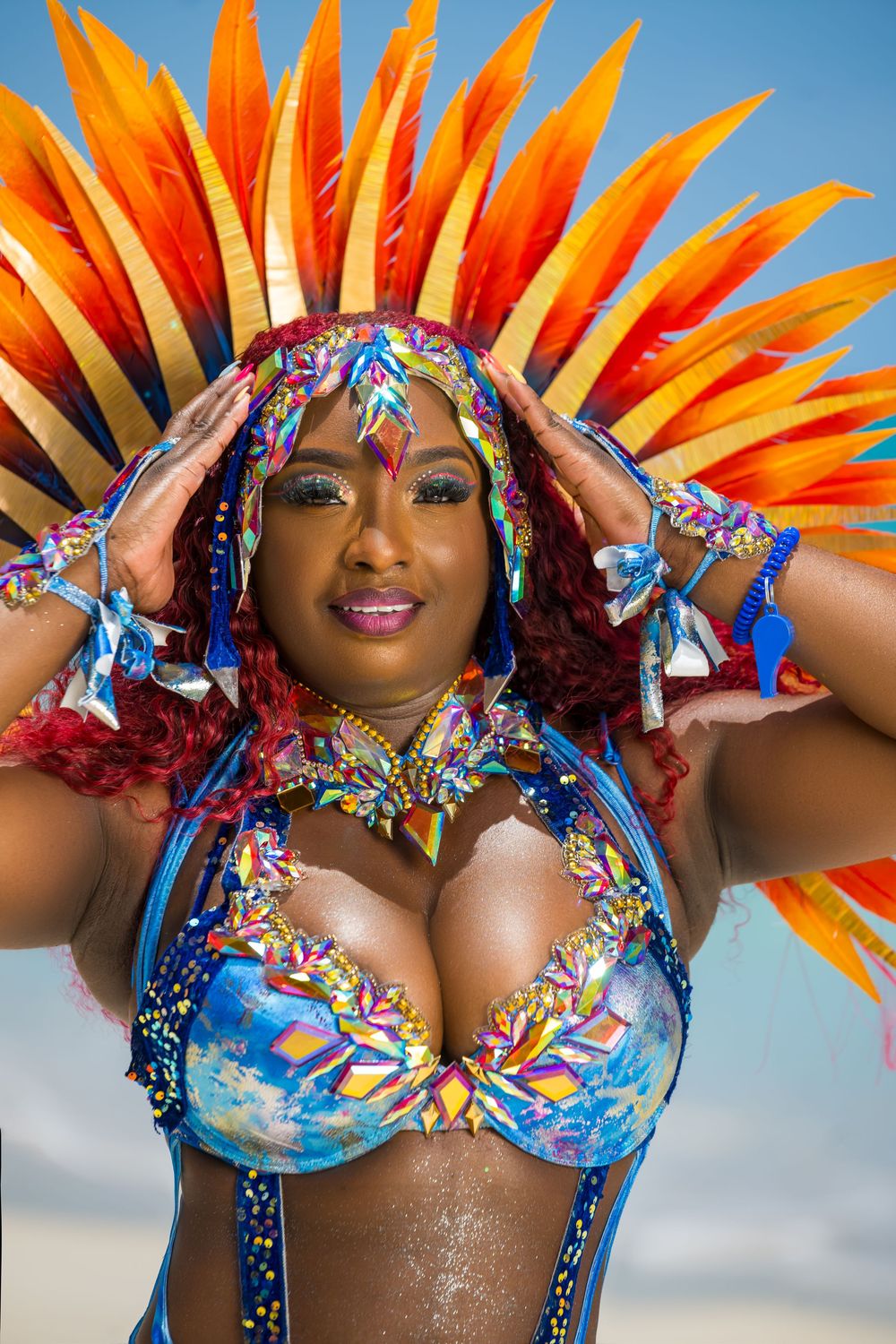Close-up of carnival dancer wearing vibrant orange feathered headdress and colorful costume.