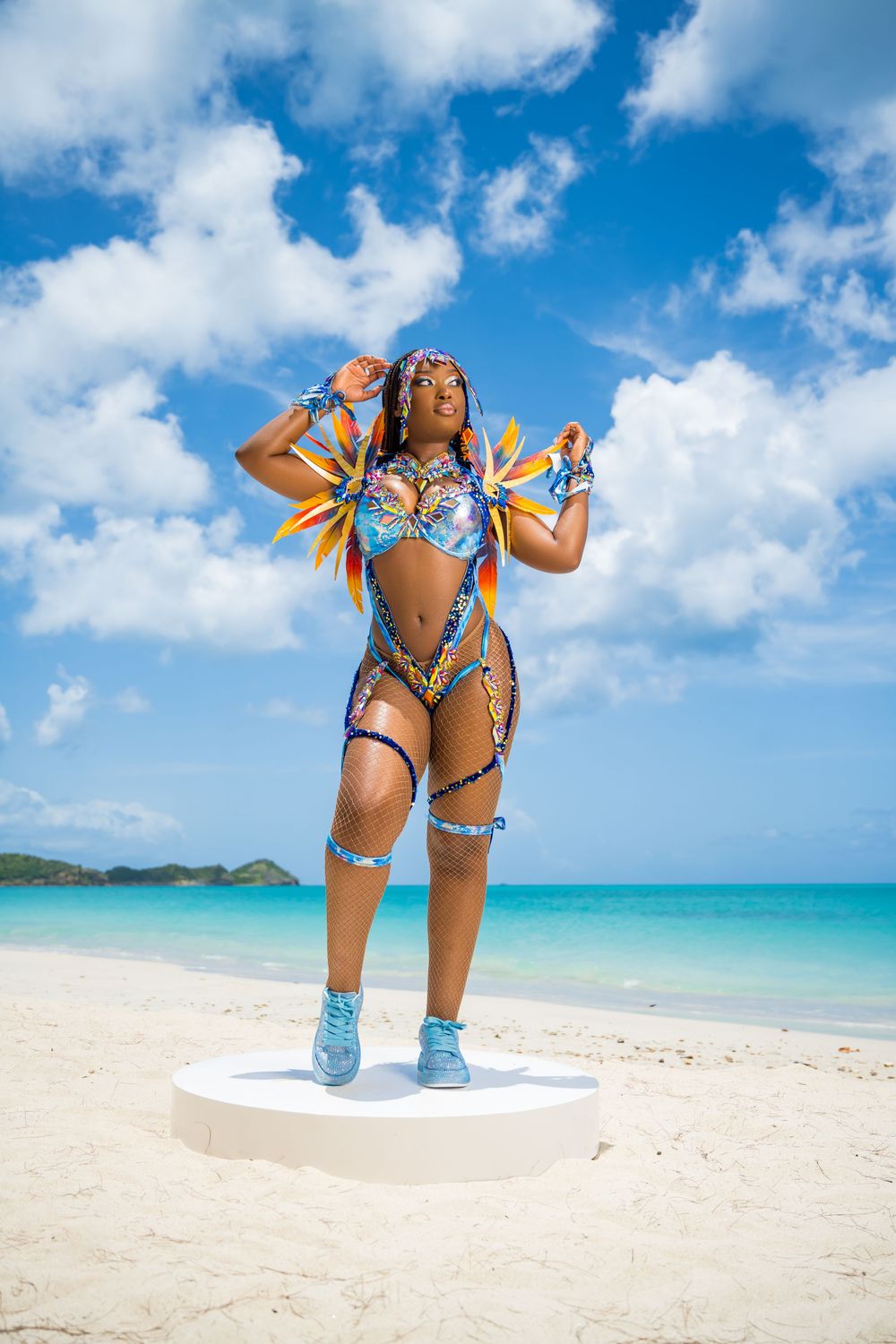 Dancer in blue sequined carnival costume performs on beach platform.