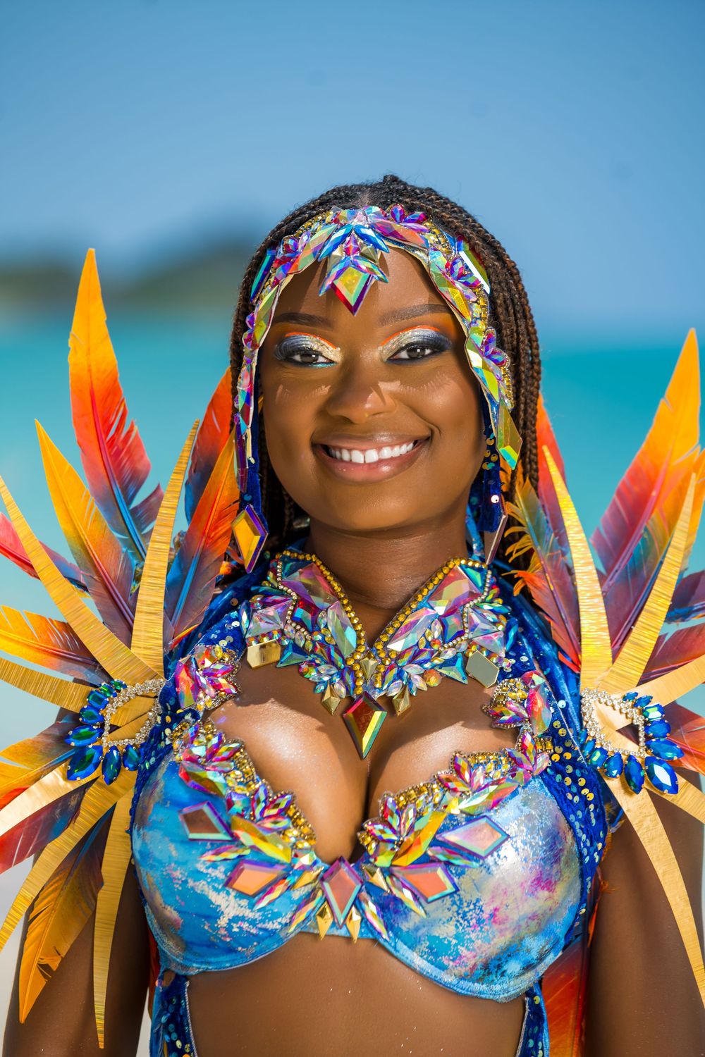 Vibrant carnival costume with colorful feathers and crystal details against tropical ocean background.