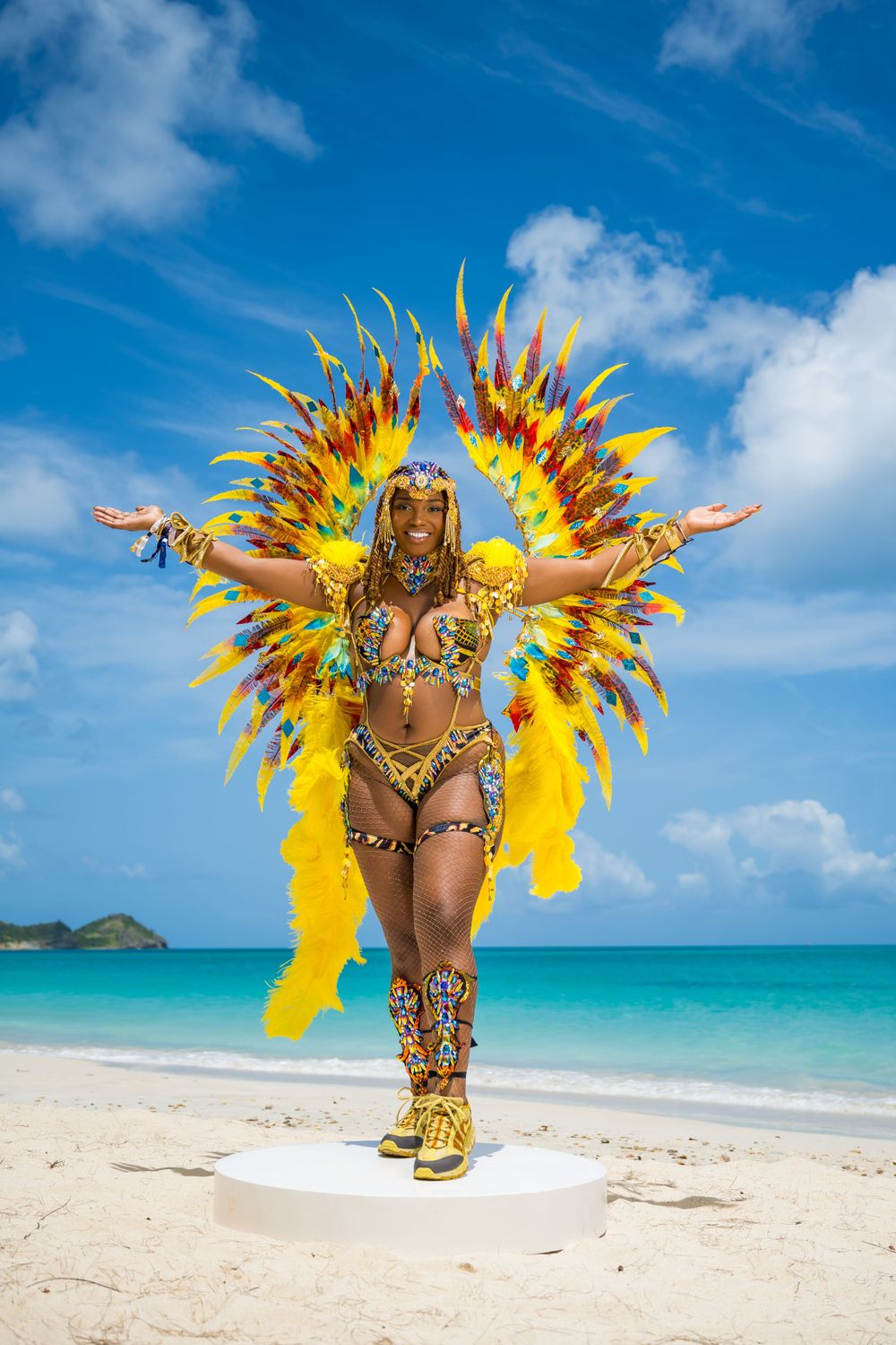 Carnival dancer in elaborate yellow and gold costume performs on beach platform.