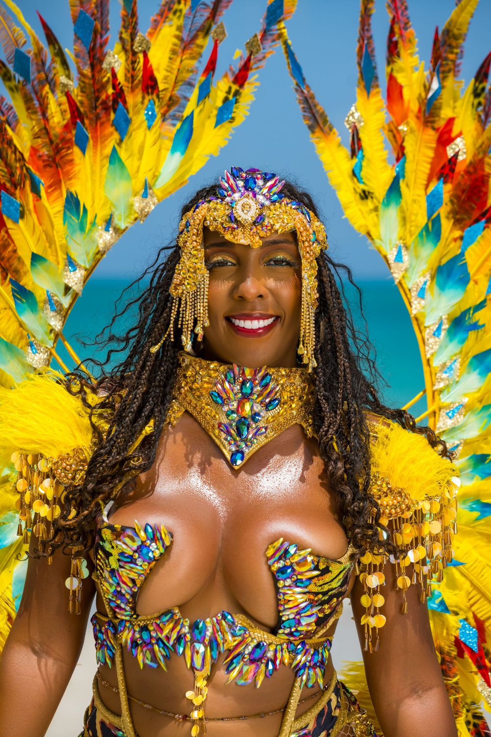 Colorful Caribbean carnival costume with yellow feathers and jeweled headpiece against blue sky.