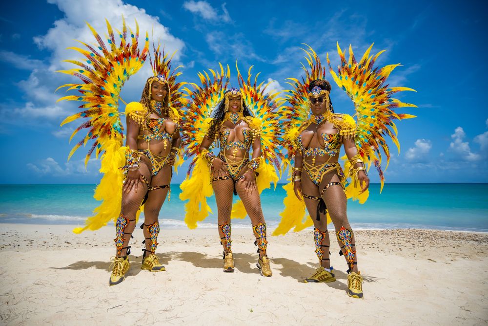 Three carnival performers in matching gold and yellow feathered costumes pose on beach.