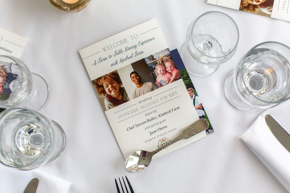 Foster care fundraiser flyer displayed on white tablecloth with empty wine glasses.