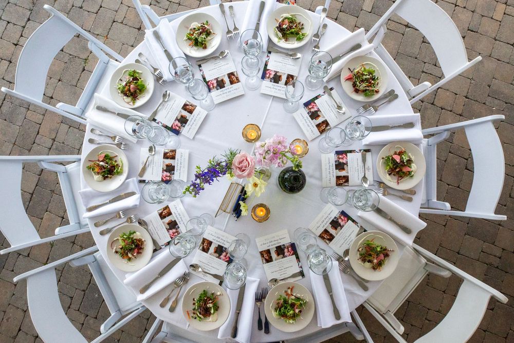 Overhead view of an elegant round table setting with white chairs and plated meals.