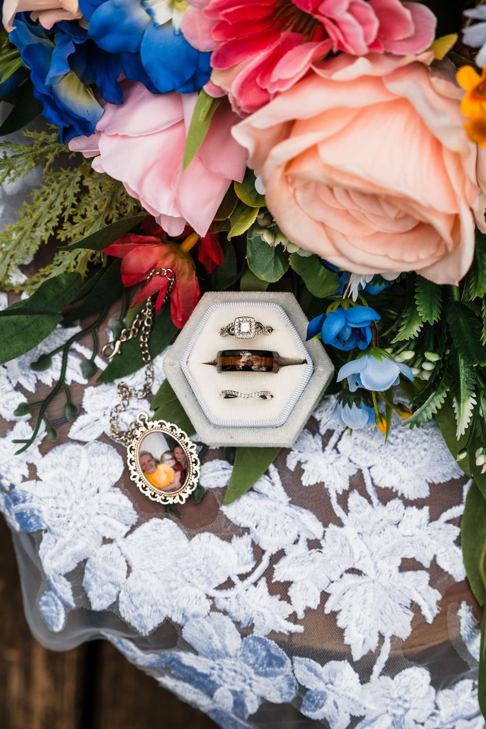 Wedding ring in hexagonal box with pink and blue flowers on white lace against wooden surface.