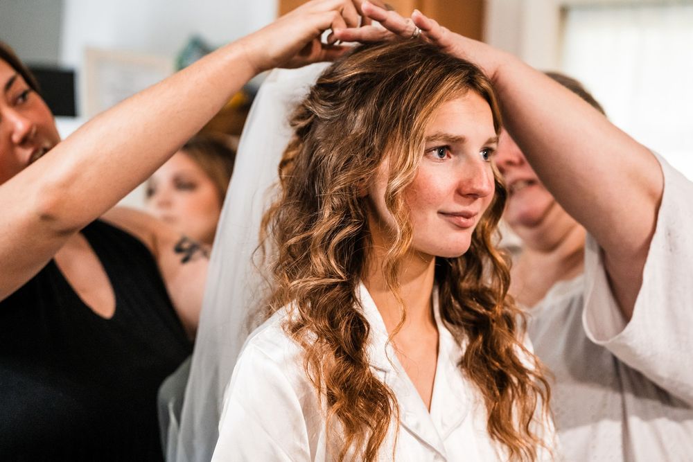 Wedding preparation moment showing final touches being added to bridal hair and veil.