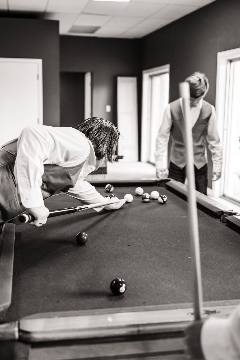 Two people playing pool in a dimly lit room during what appears to be a wedding celebration.