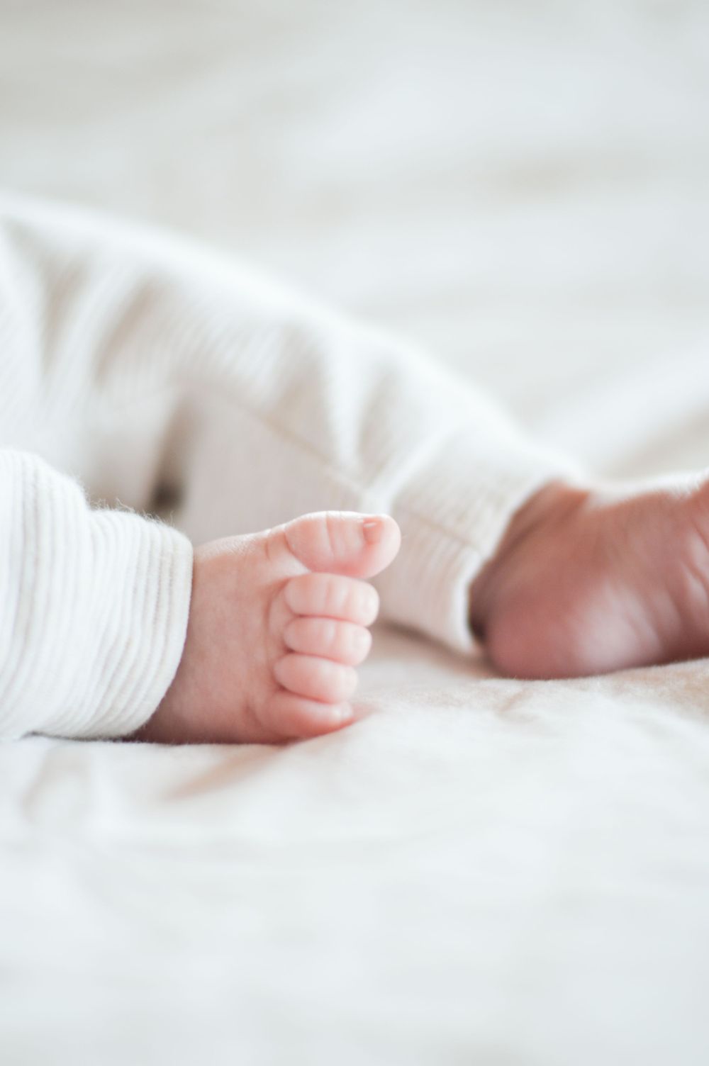 Nahaufnahme von winzigen neugeborenen Babyfüßen mit weißen Socken auf weicher weißer Bettwäsche.