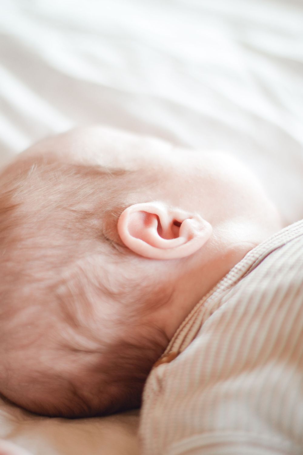 Nahaufnahme des Ohrs eines Babys auf weicher Bettwäsche, die die feinen Details der äußeren Ohrstruktur zeigt.