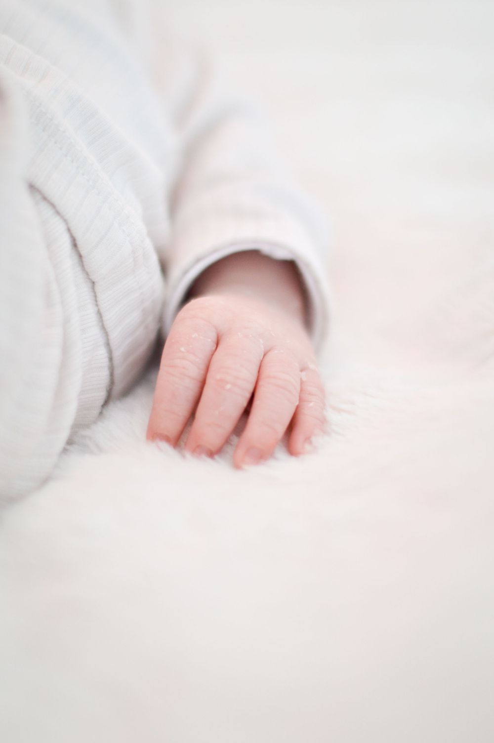 Die Hand eines Babys ruht zart auf einem weichen, weißen Bettchen.