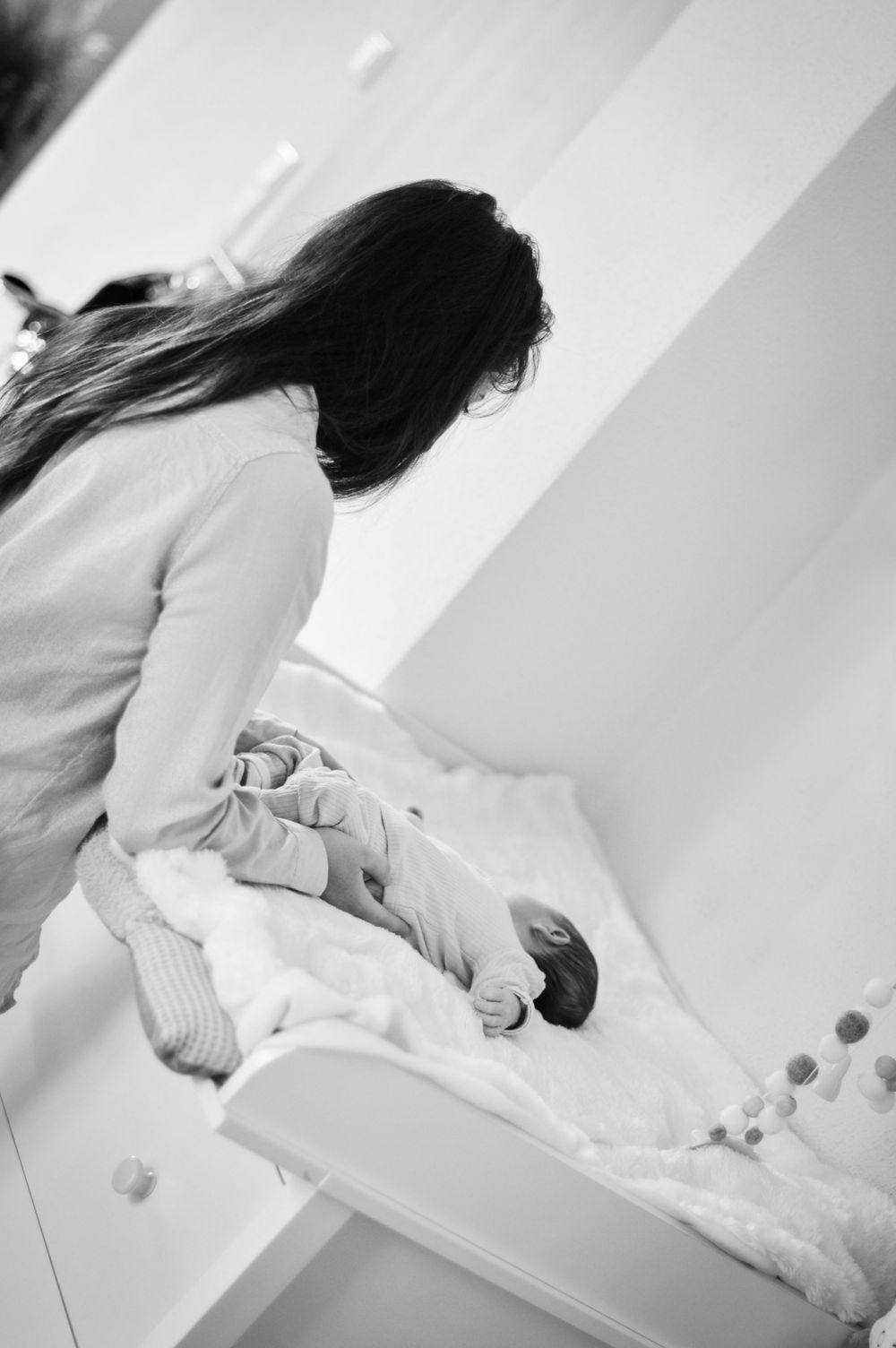 Ein zärtlicher Moment zwischen Mutter und Baby am Wickeltisch in einem lichtdurchfluteten Raum, festgehalten in schwarz-weiß.