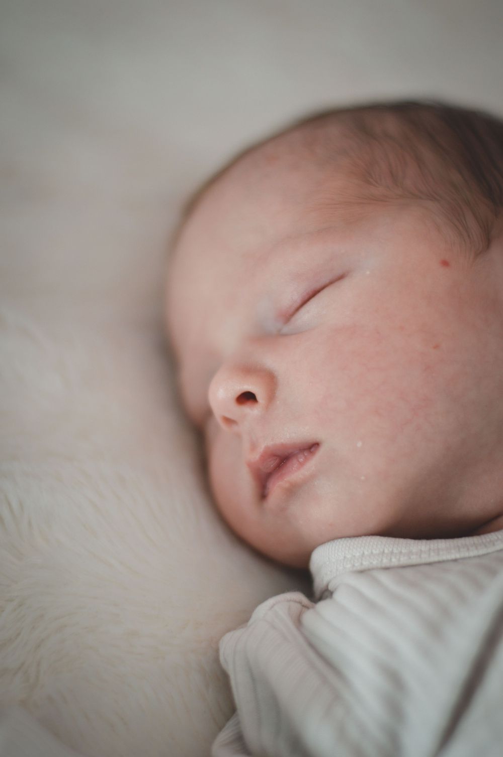 Ein kleines Baby schläft friedlich auf einem weichen weißen Bettchen in einer sanften Nahaufnahme.