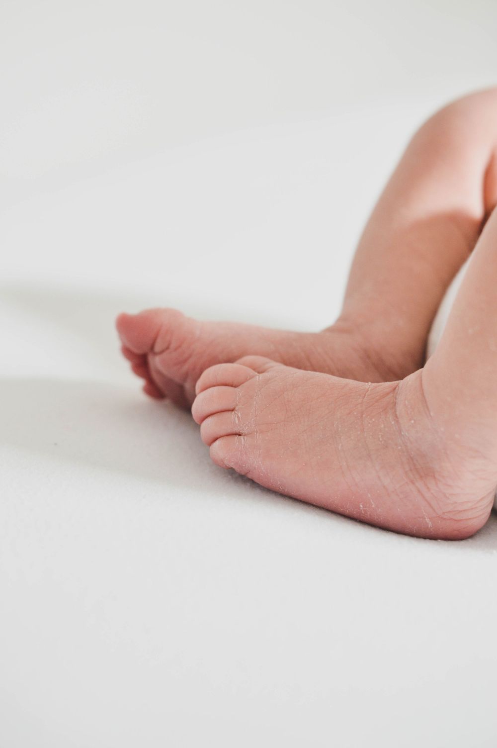 Nahaufnahme von winzigen Babyfüßen, die auf einer weißen Fläche ruhen und zarte Zehen und weiche Haut zeigen.
