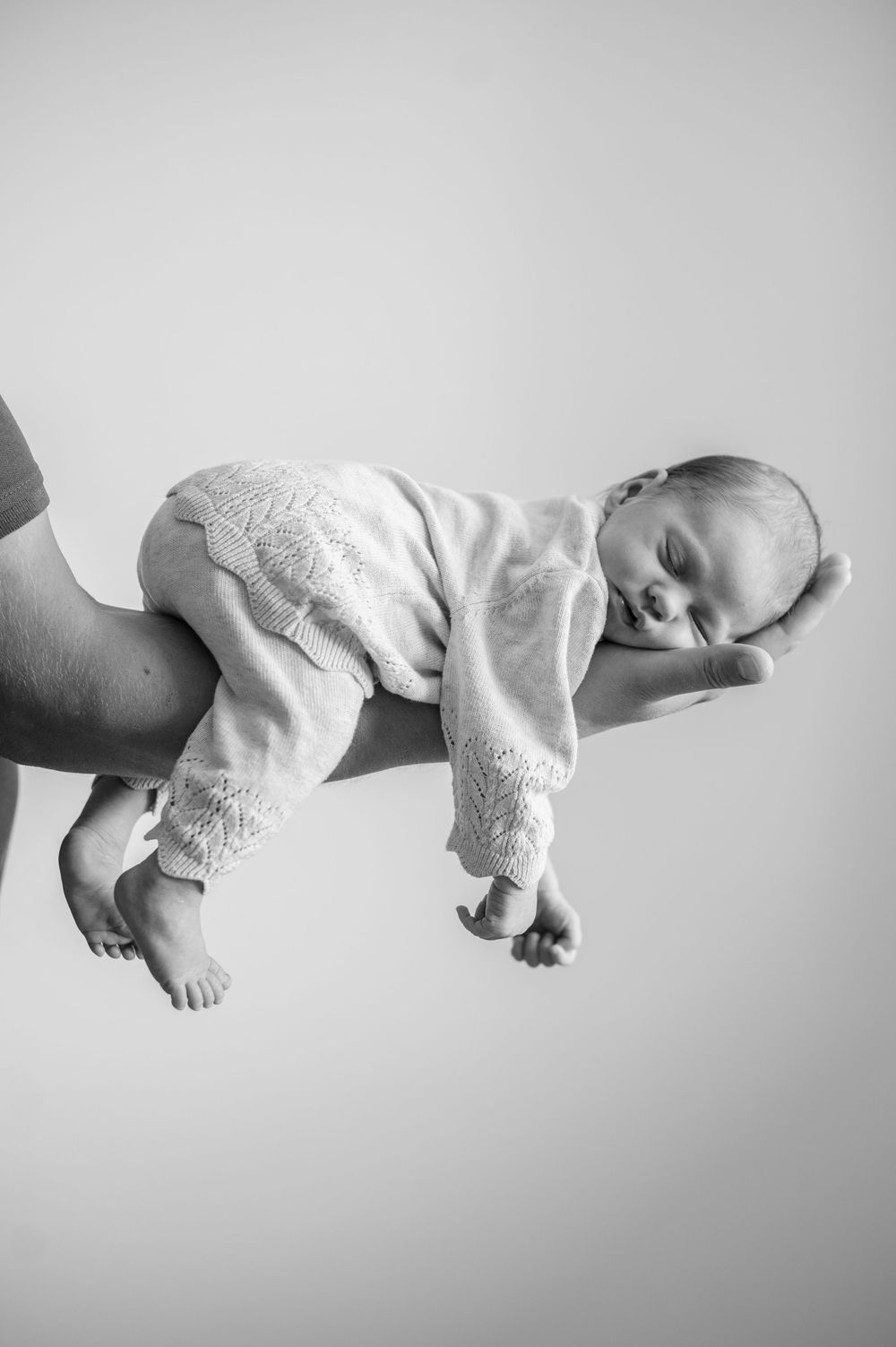 Schwarz-weiß Aufnahme eines schlafenden Babys im Fliegergriff auf dem Arm des Papas