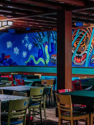 Vibrant restaurant interior with colorful wall murals featuring sea creatures and tribal designs alongside dining tables.