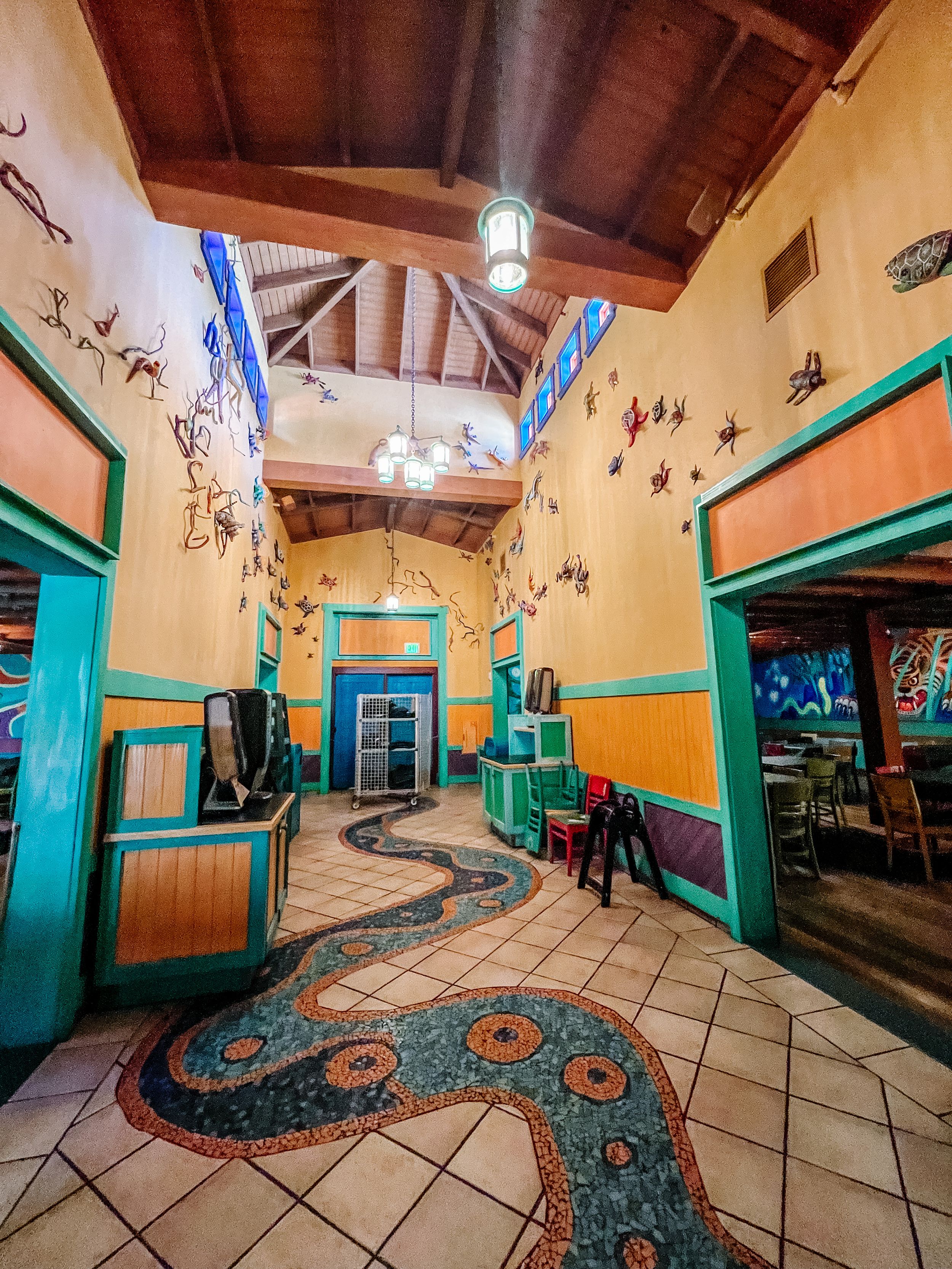 A detailed view of a decorative mosaic snake path winding through a building's tiled floor with turquoise bench seating.
