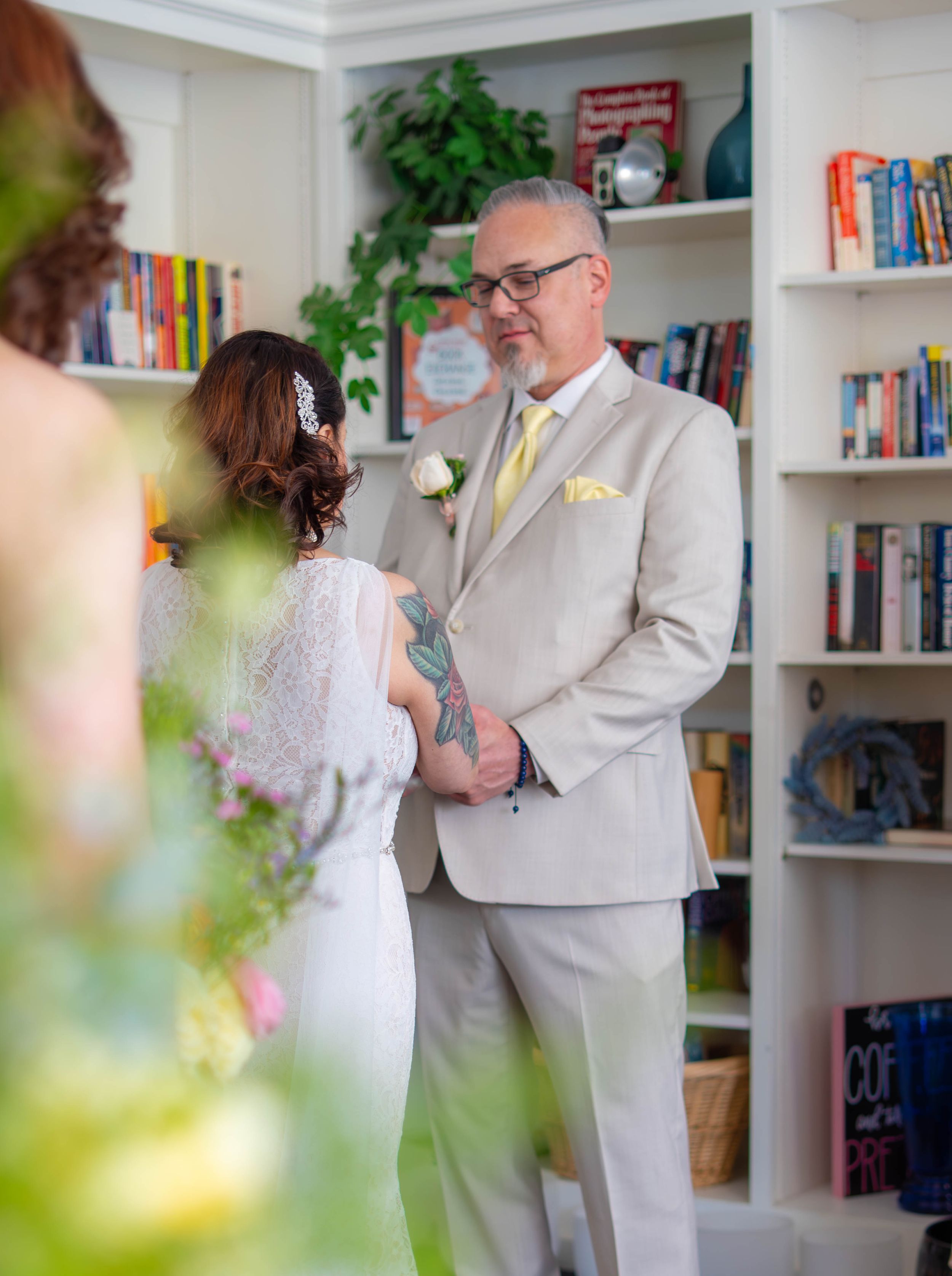 A small intimate wedding ceremony takes place in a cozy home library with bookshelves and plants as the backdrop. Quad Cities Wedding Photo