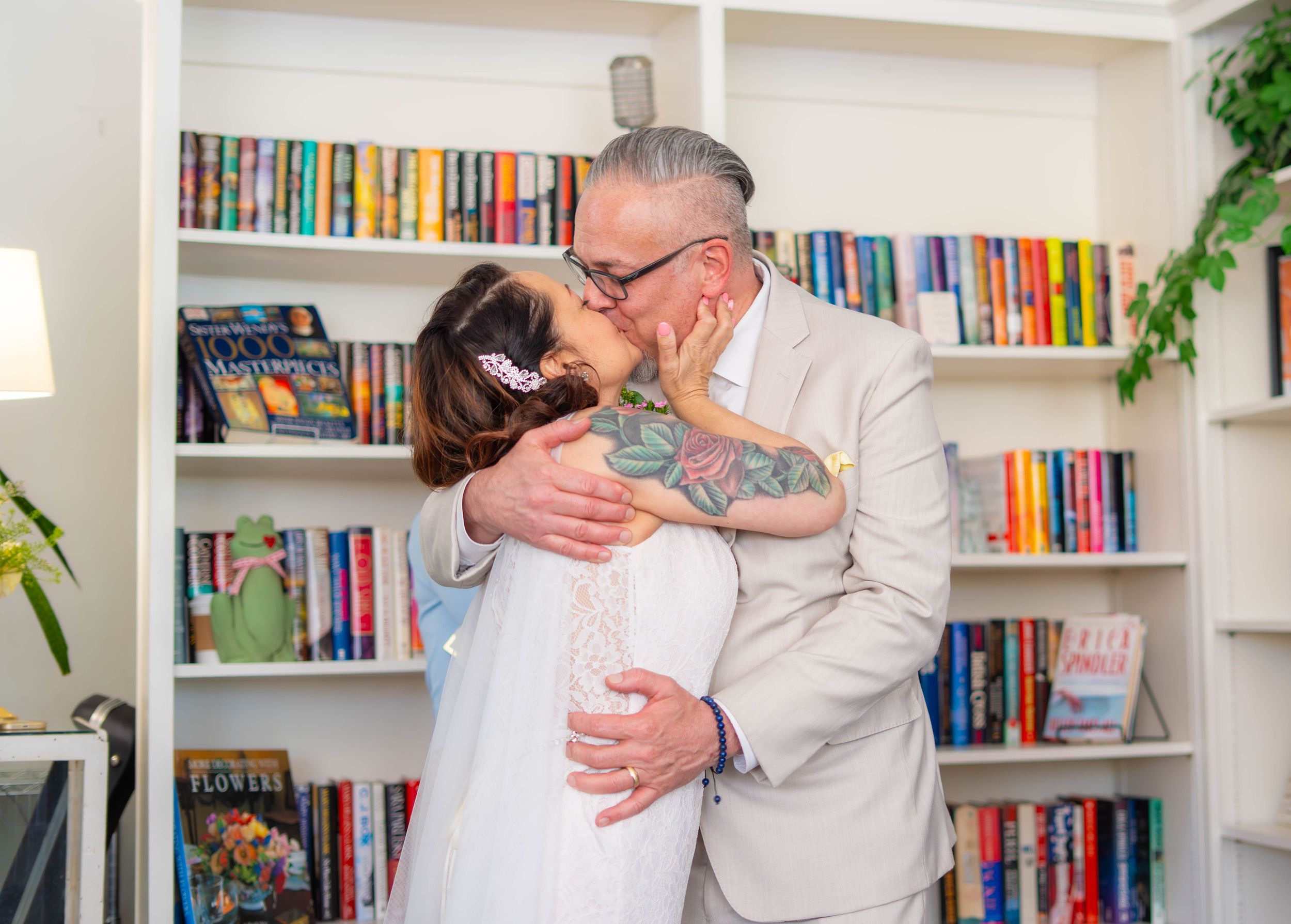 A couple embraces and shares a tender moment in front of a colorful built-in bookshelf in a home library setting. Quad Cities Wedding Photog