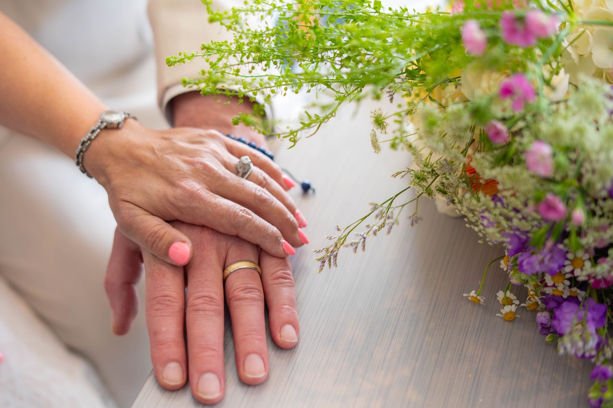 A close-up of hands with an engagement ring beside colorful wildflowers on a white surface. Quad Cities Wedding Photography