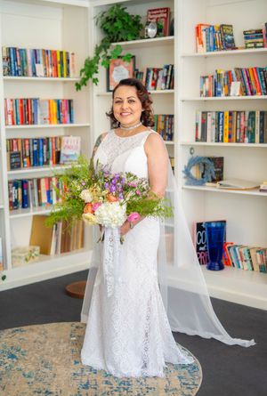 Quad Cities Wedding Photography. Bride in white lace wedding dress holds a colorful bouquet while standing in front of built-in bookshelves.