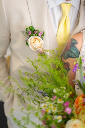 A delicate peach rose and greenery boutonniere pinned to a cream suit jacket with a yellow tie. Quad Cities Wedding Photography