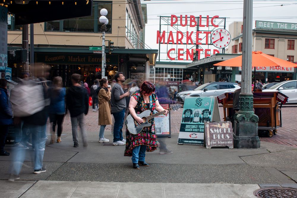 Public Market Center sign with busy street scene and pedestrians in motion blur except for guitarist perfectly in focus.