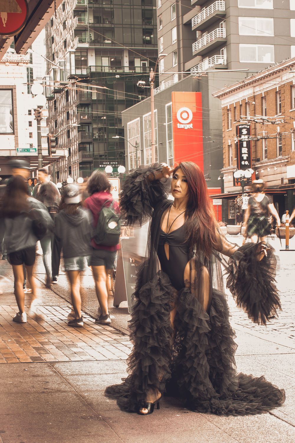 A person in a dramatic black flowing dress that billows on a city street in front of motion blurred crowd.
