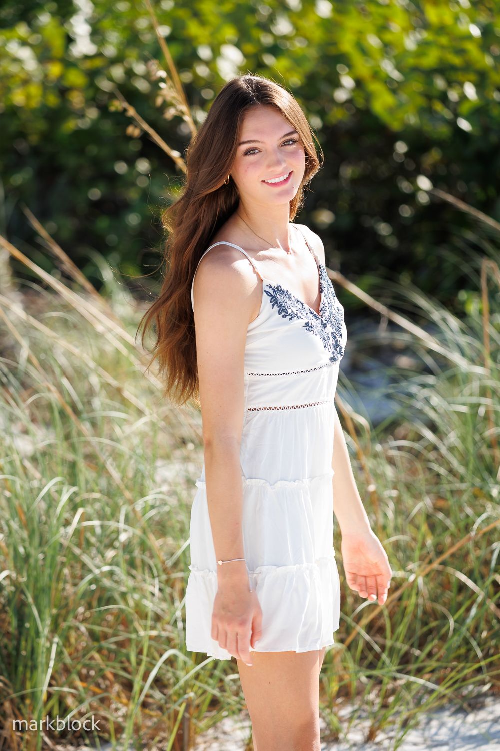 A summer portrait outdoors featuring a white sundress against a natural backdrop of tall grass and greenery.