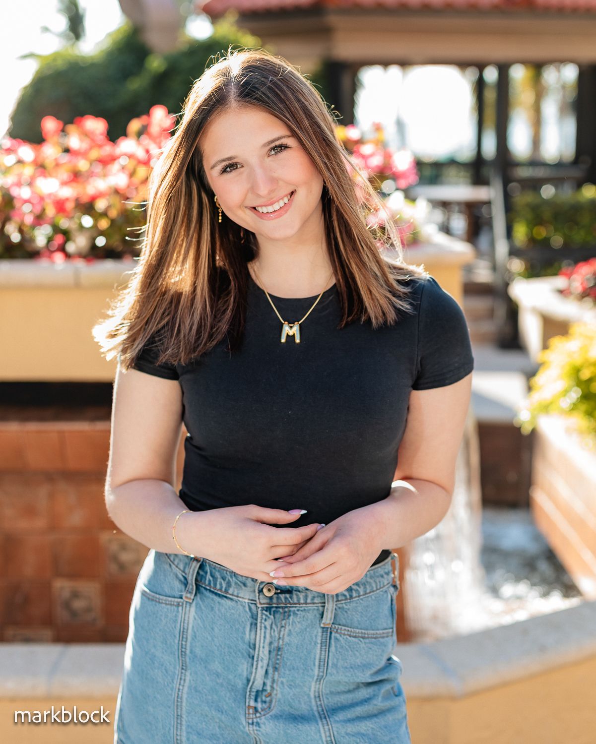 A person wearing a black t-shirt and jeans stands in front of colorful flowers and Spanish-style architecture.