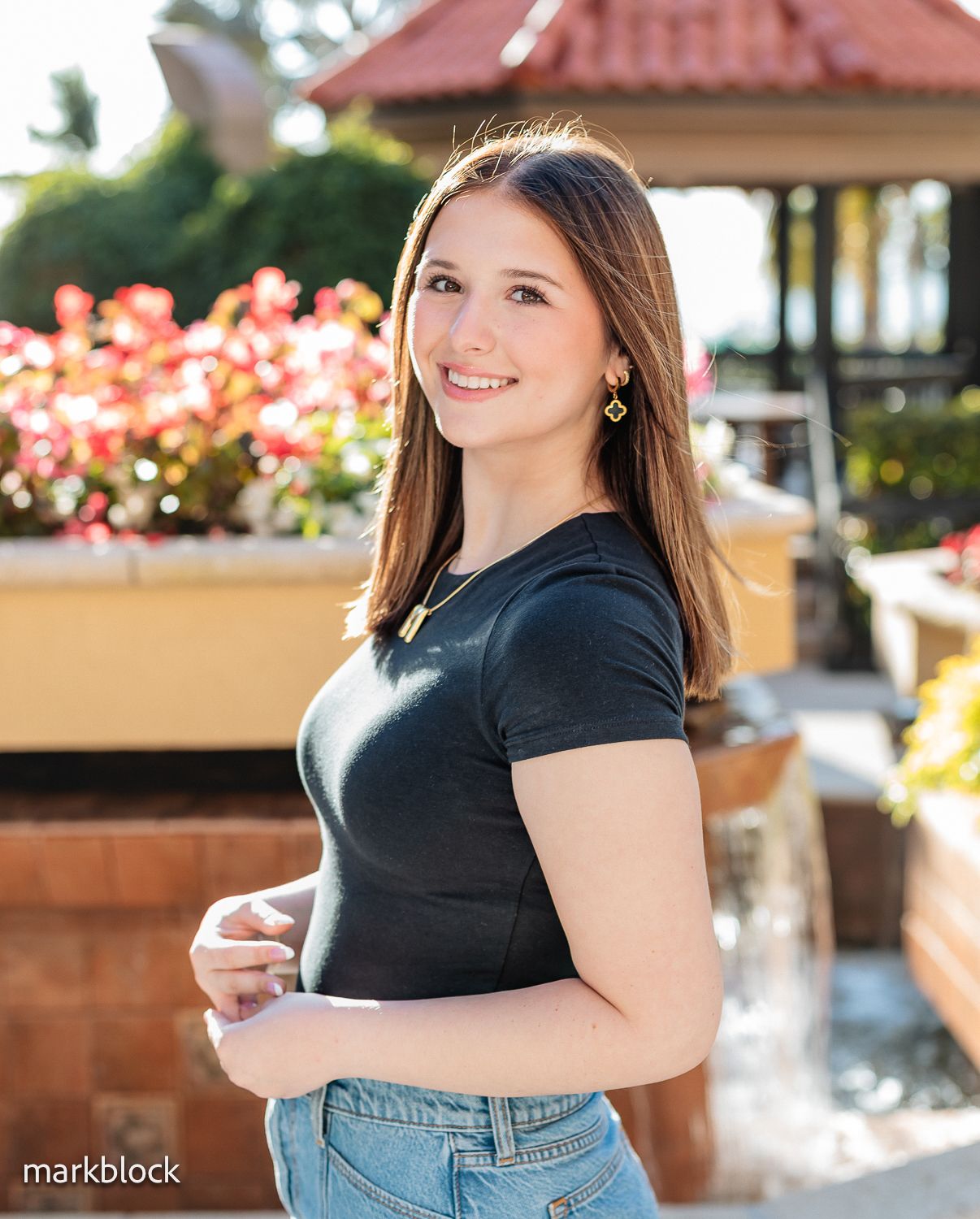 A casual portrait features dark straight hair and a black t-shirt against a garden backdrop with pink flowers.