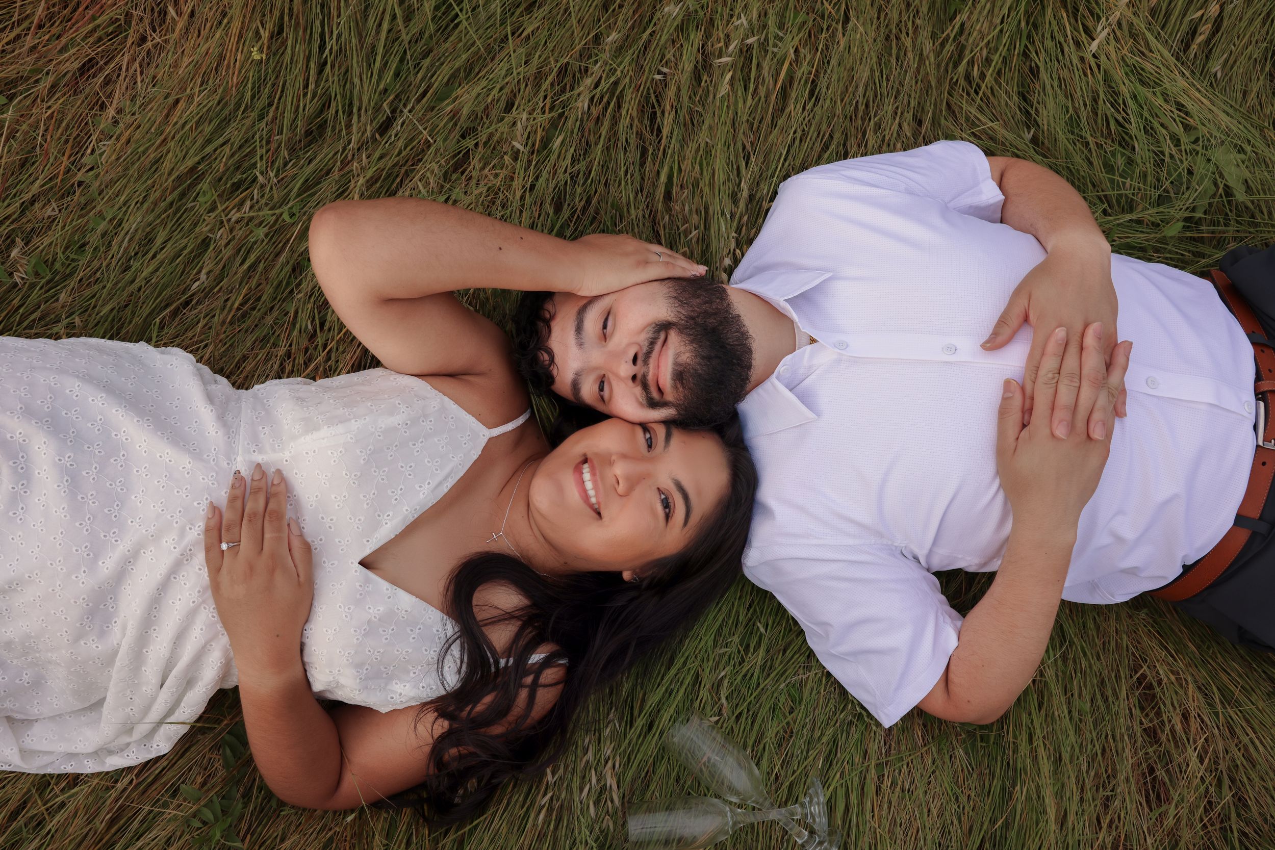 Person wearing white dress lying on grassy field in artistic poses during outdoor photo session.
