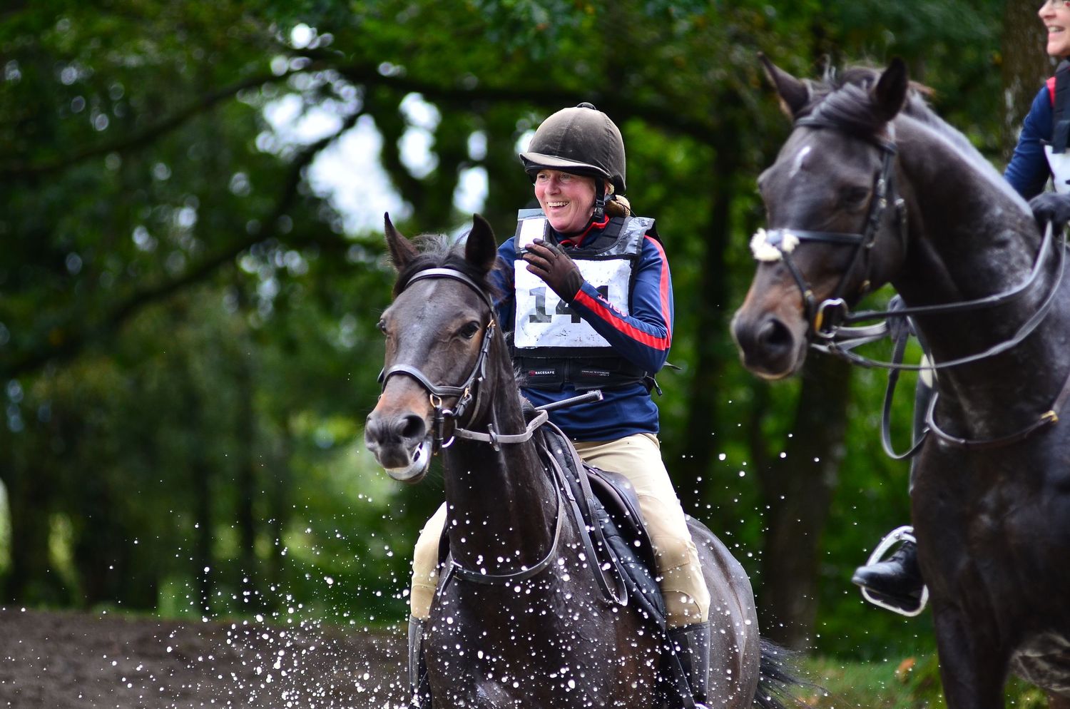 Horses and riders splash through water during a competitive cross-country event.