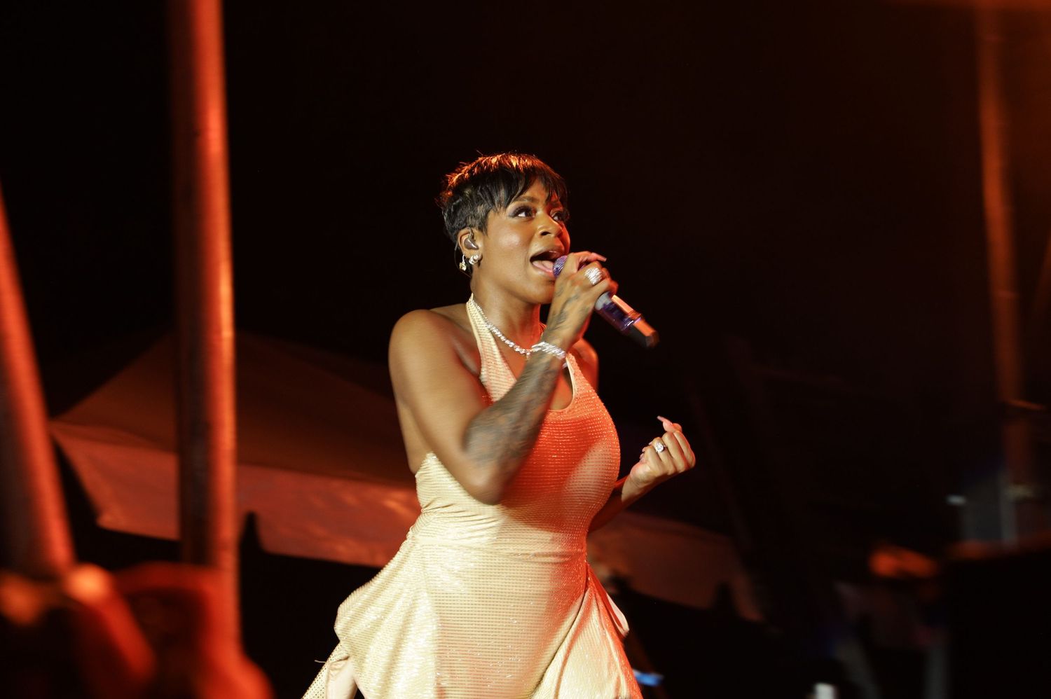 A performer in a white sleeveless dress sings passionately on stage under dramatic red lighting.