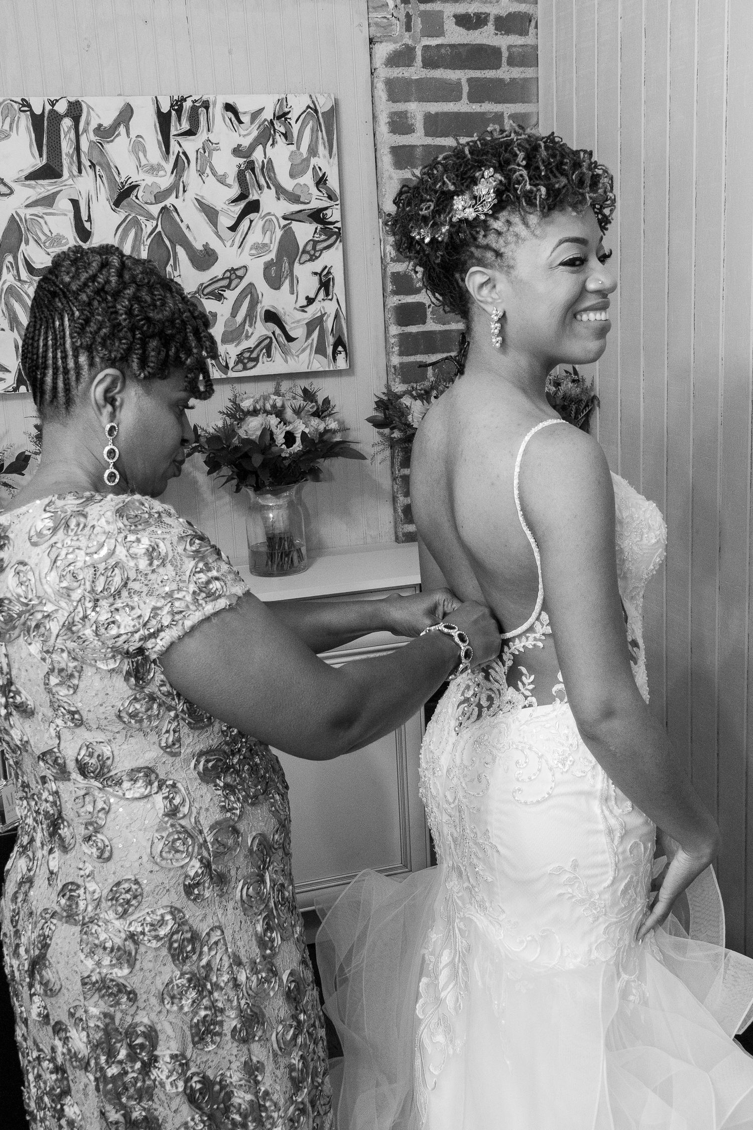 Black and white photo showing final wedding dress fitting as an attendant helps adjust the elegant lace gown.