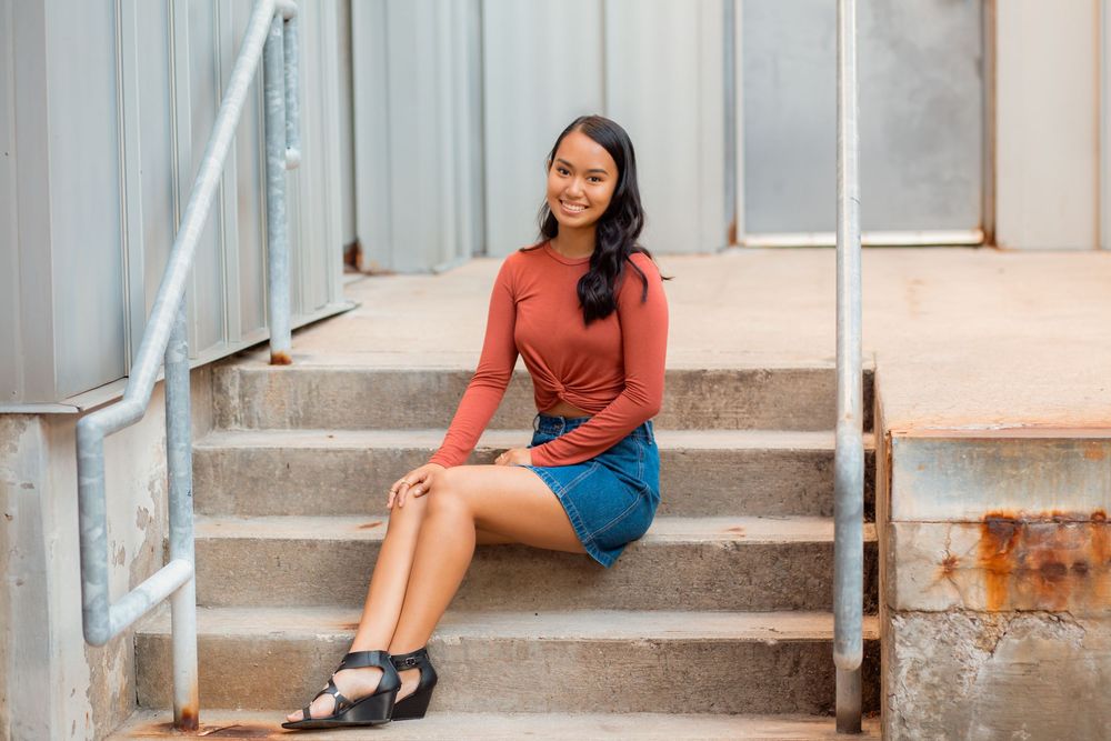 A person sits casually on concrete steps wearing a coral top and denim shorts.