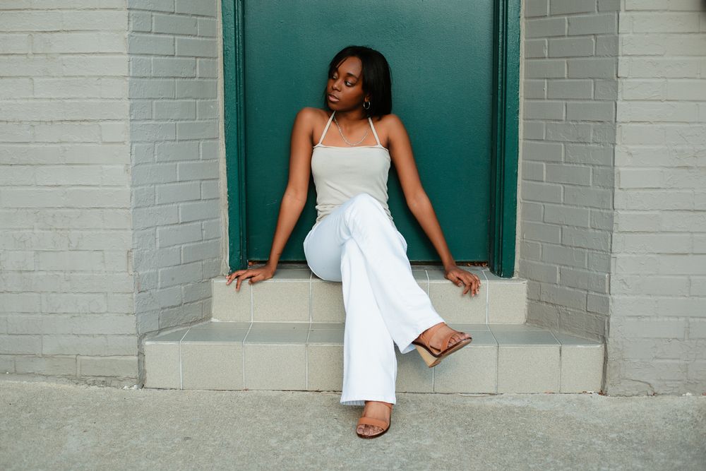 Woman in white dress poses against teal brick wall in urban setting.
