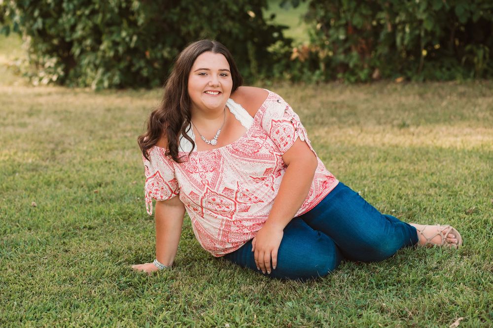 Person in coral top lounges on grass during outdoor photo session.