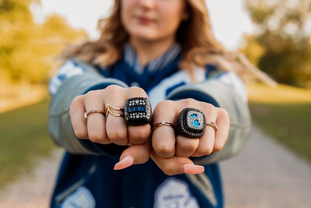 Close-up shot of hands displaying championship rings against outdoor background.