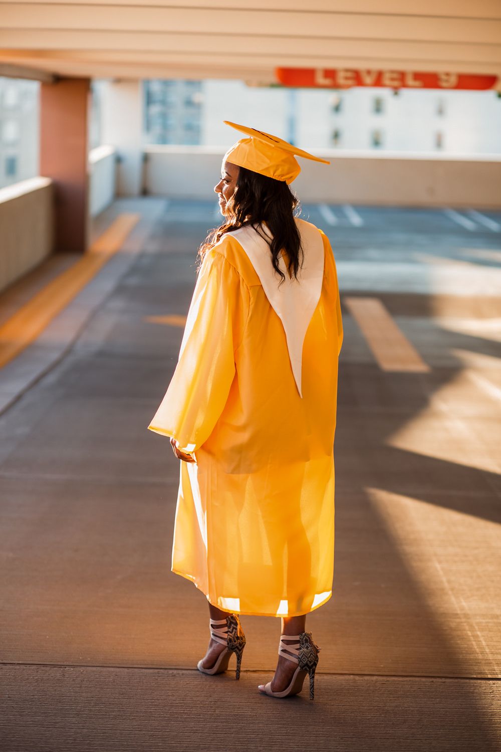 Fashion model in bright orange dress and brown boots poses in a parking garage with dramatic lighting.